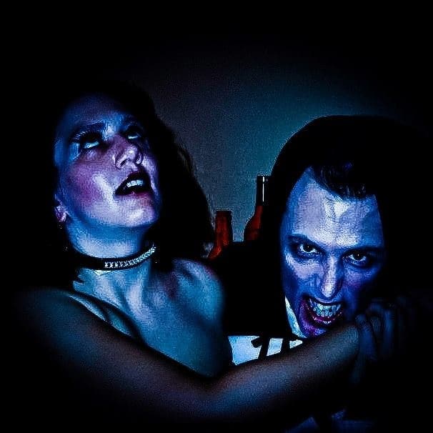 Vampire-costumed couple at indoor Halloween party, staged bite