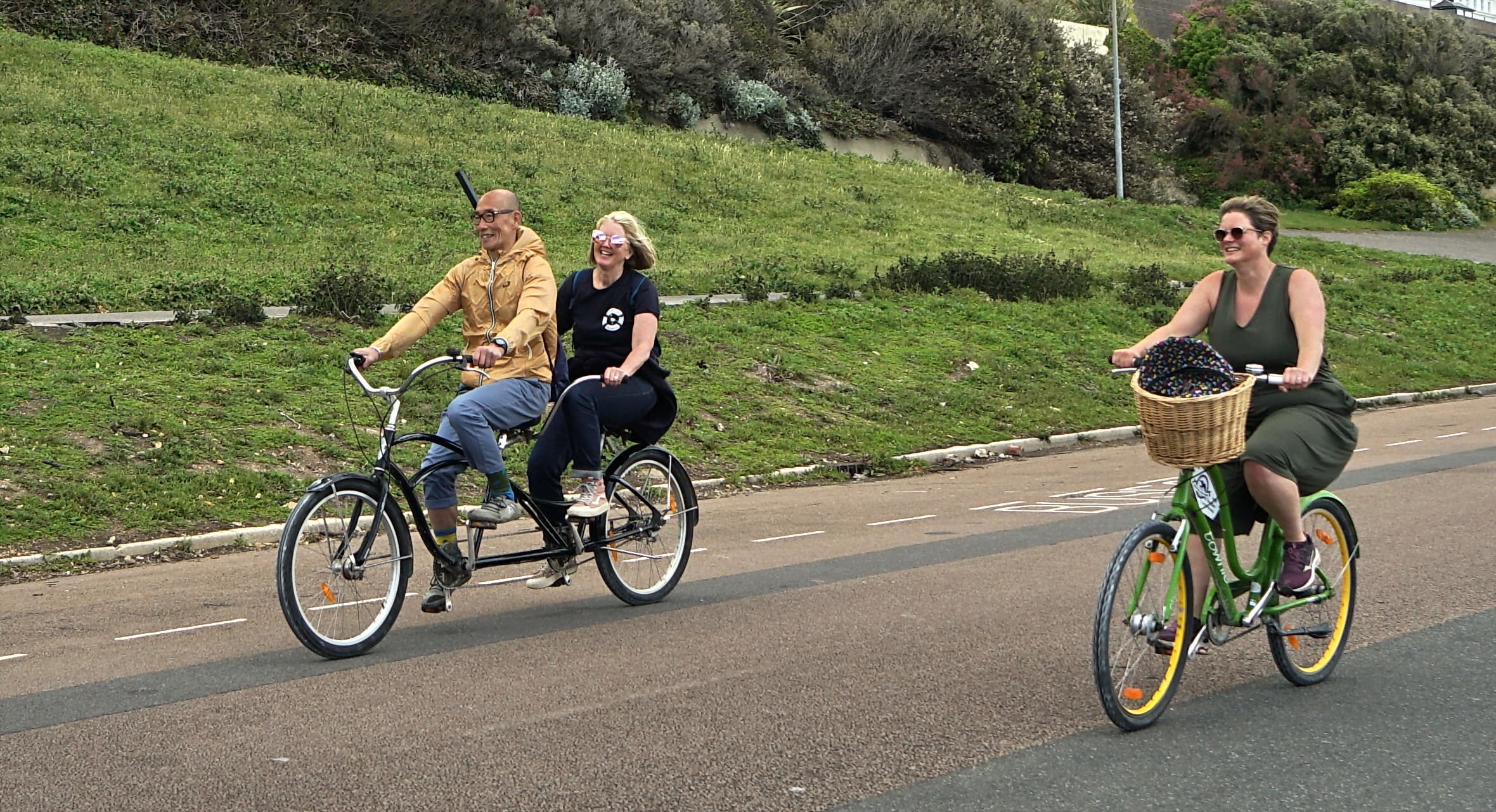 Two riders tandem and solo cyclists on coastal bike path