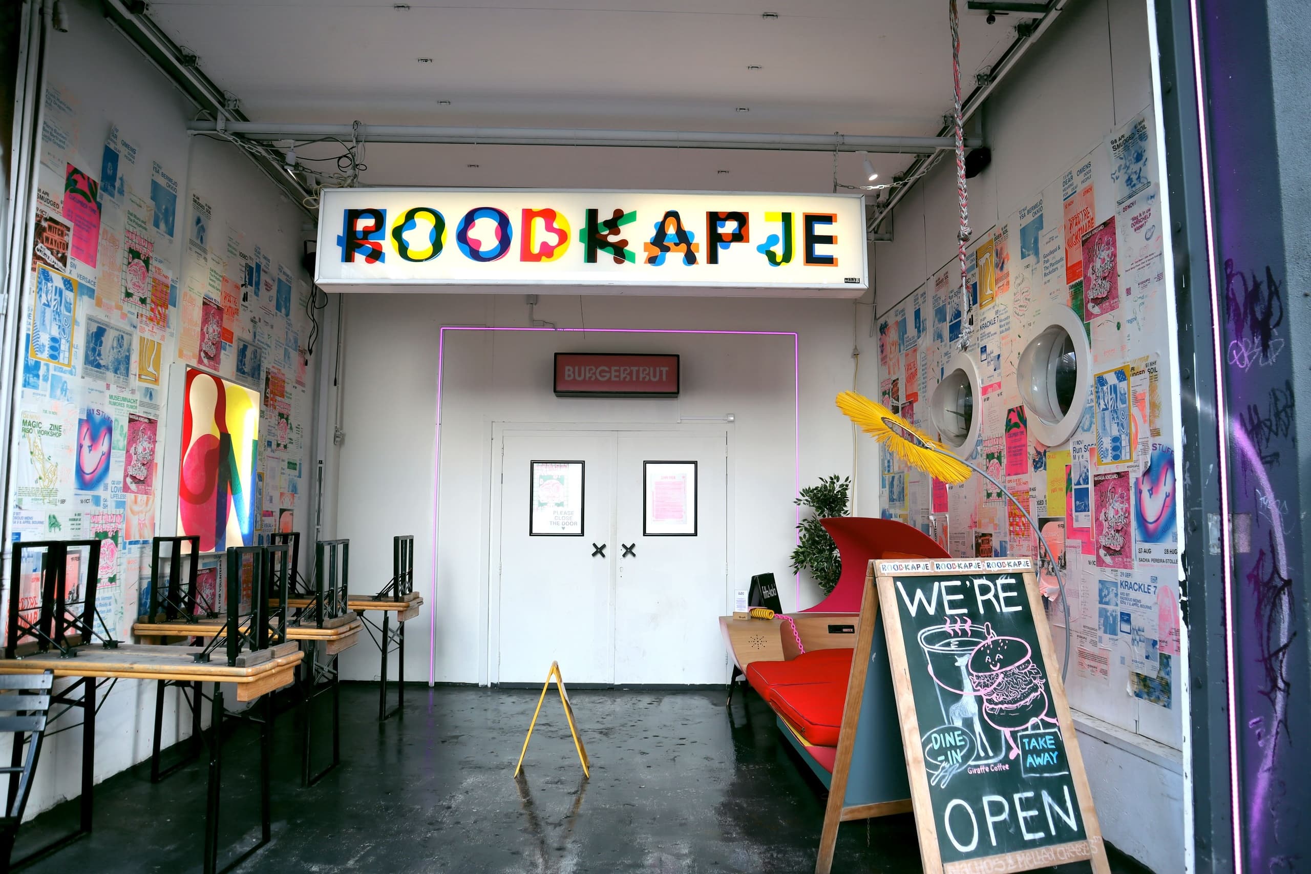 Colorful indoor pop-up space entrance with neon 'Roodkapje' sign and posters