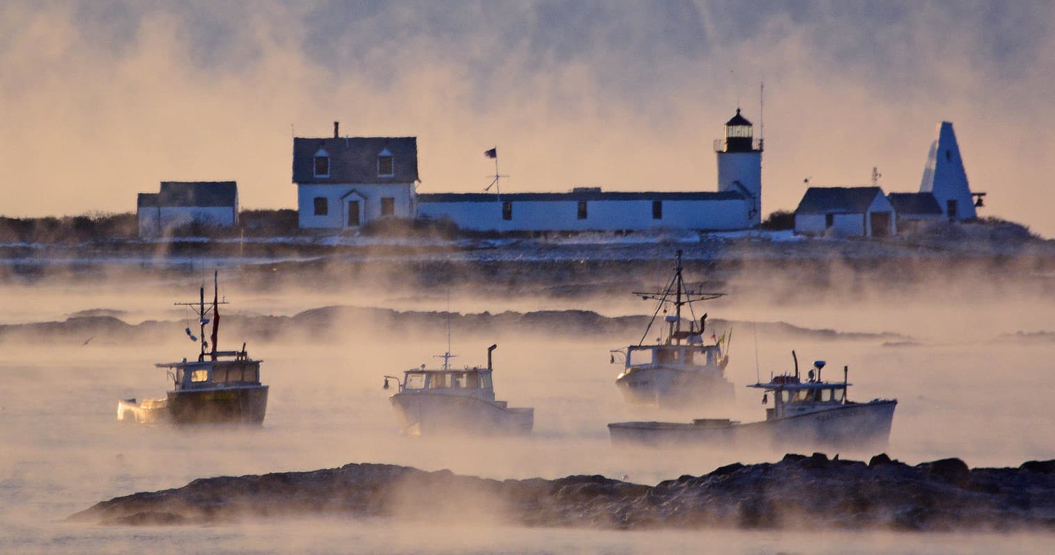 Fishing boats in morning fog near rocky lighthouse coast