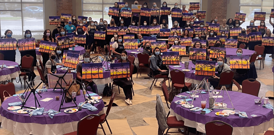 Large paint party setup in banquet hall with easel tables