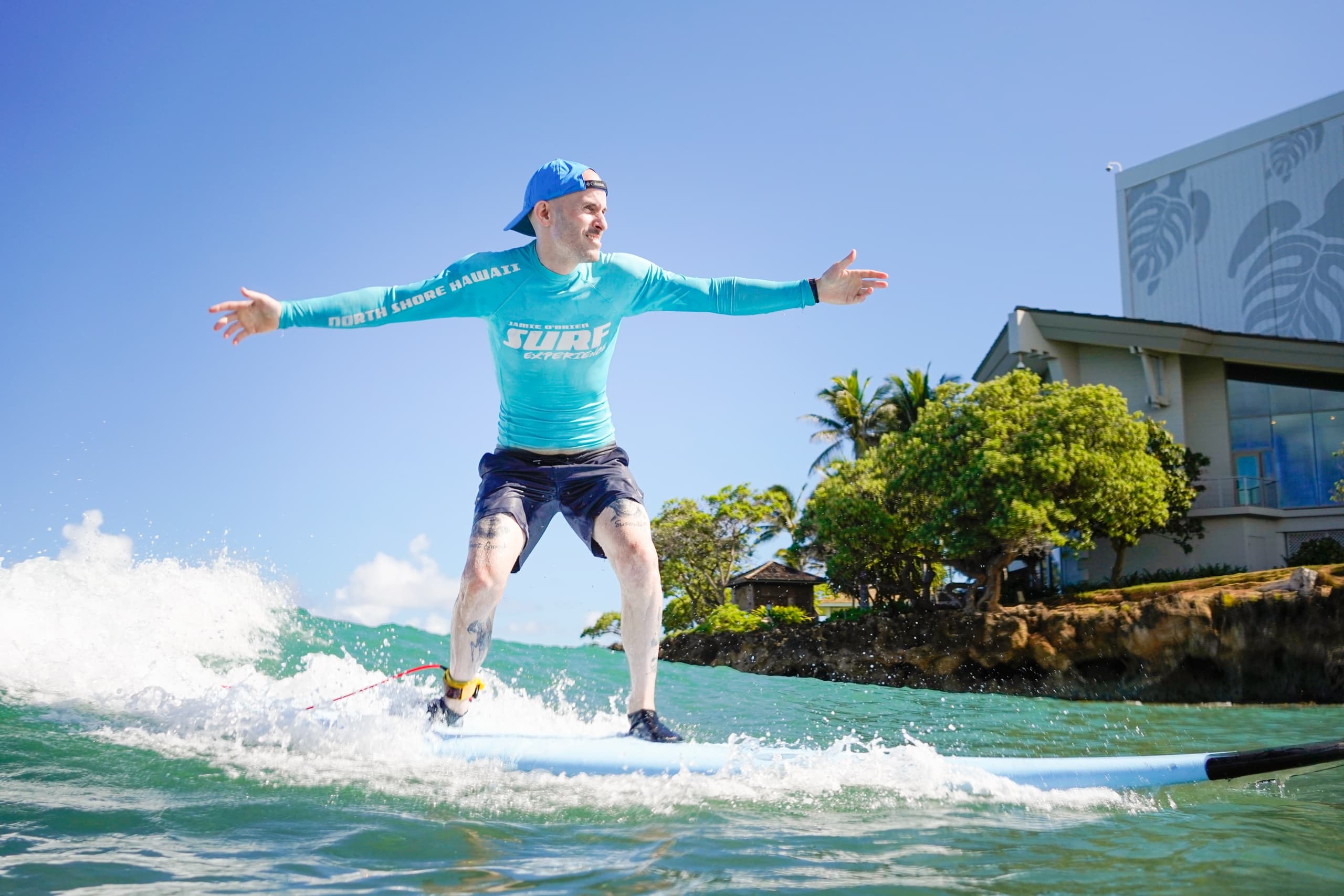 Surfer riding small wave near rocky shoreline in sunny conditions