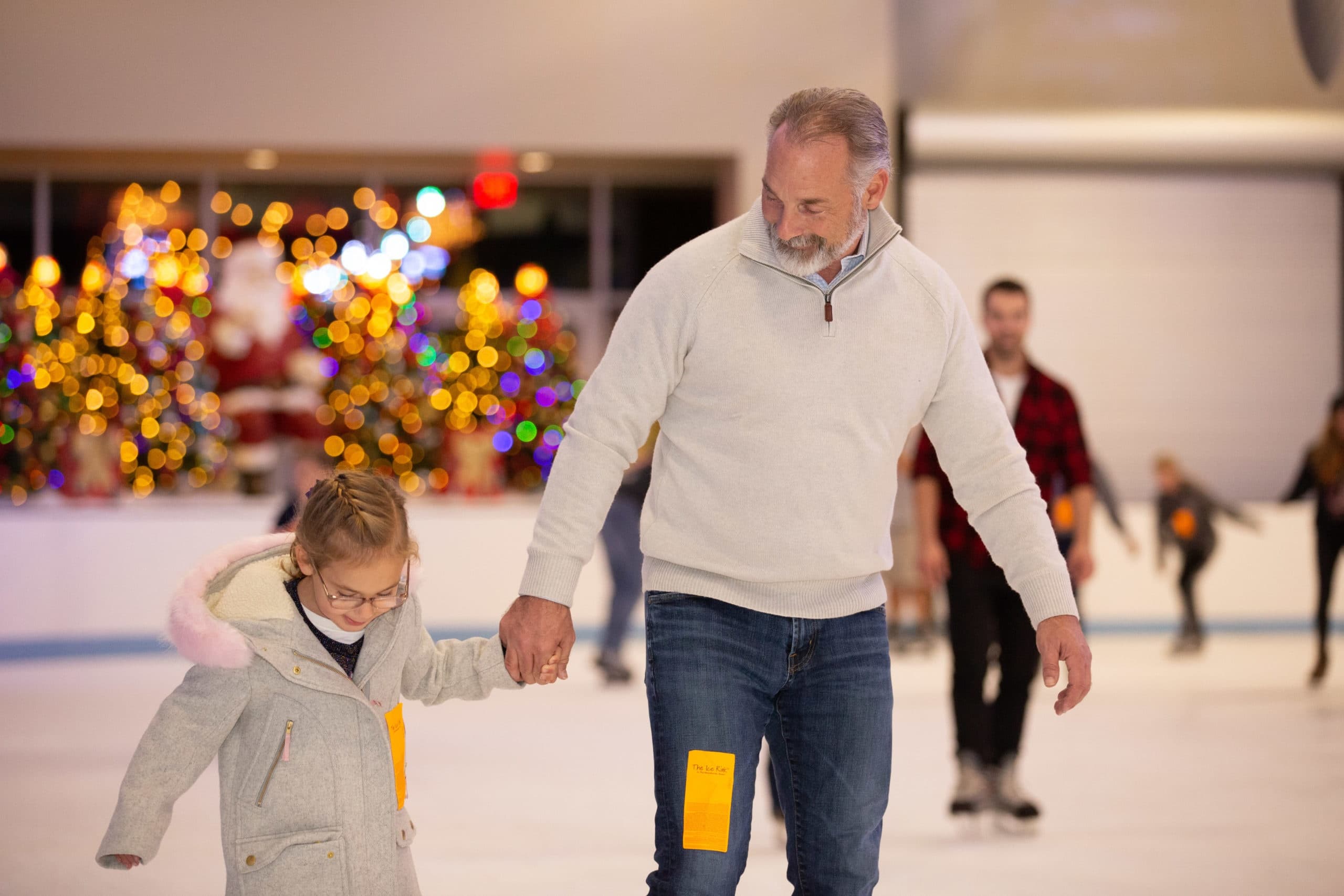 Father guiding child skating on indoor holiday ice rink