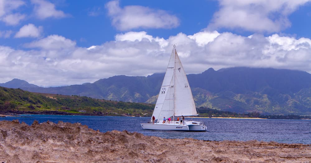 Sailboat cruising along volcanic coastline with mountain backdrop