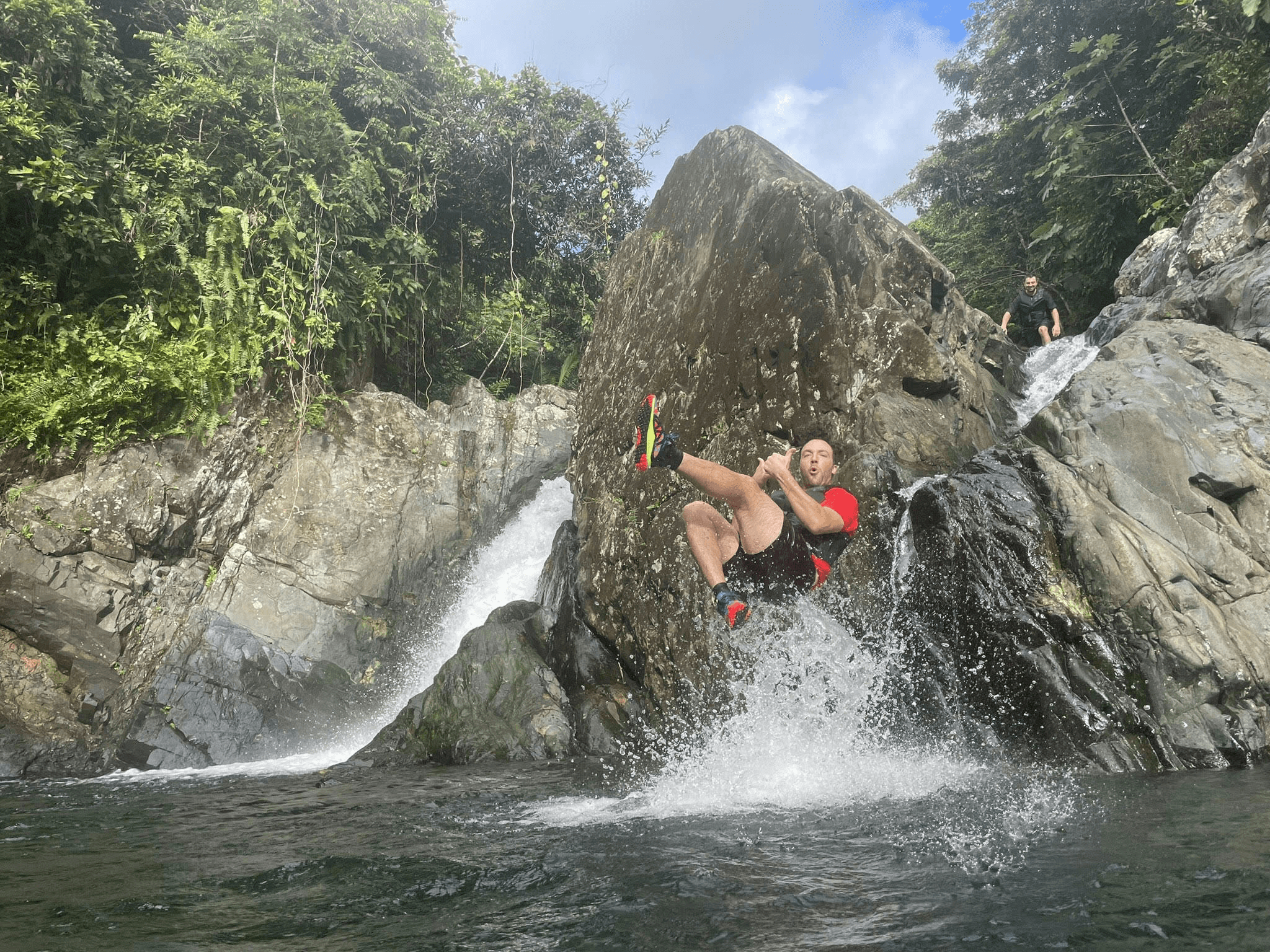 Person cliff-jumping into tropical river pool by waterfall