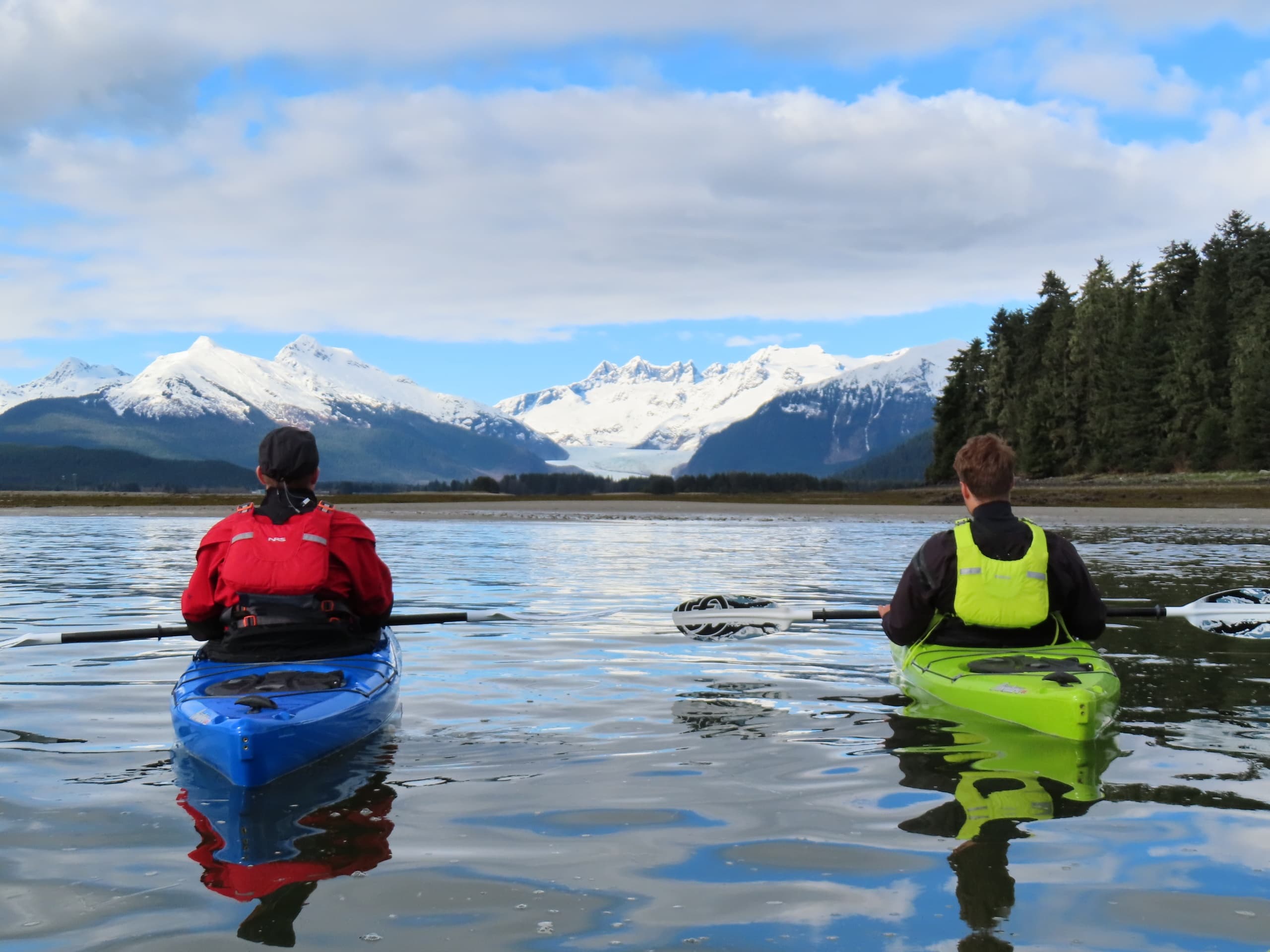 Two kayakers paddling toward snow-capped mountains in Alaska