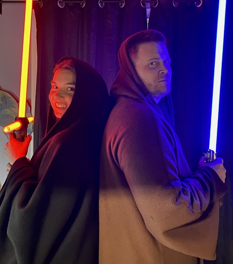 Two fans back to back wielding lightsabers in indoor photo booth