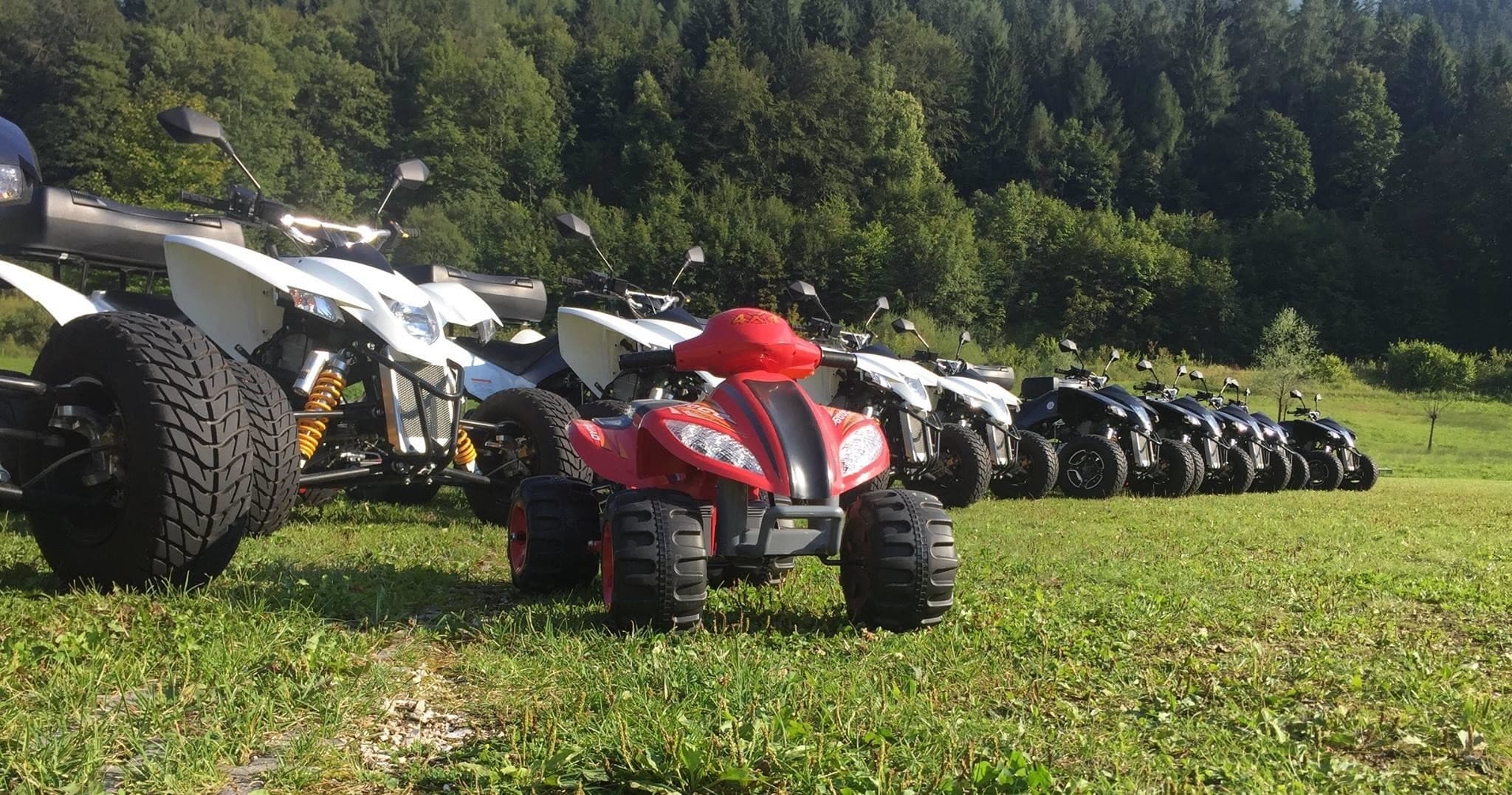 Row of ATVs parked on grassy field near forested hills