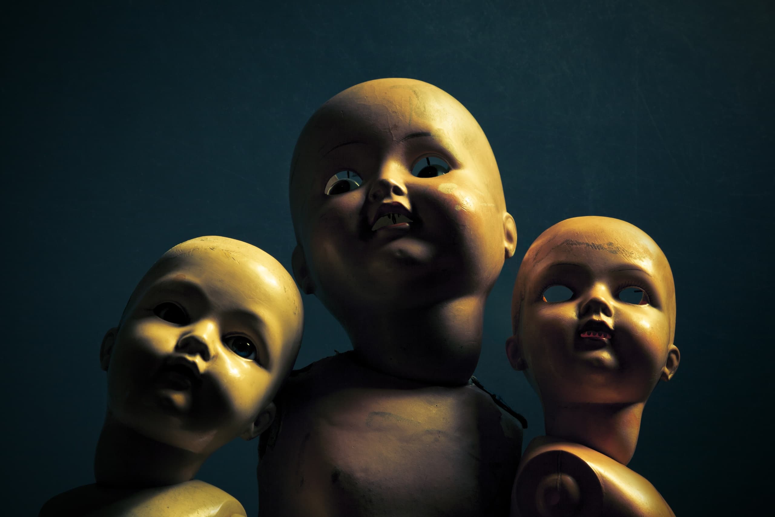 Three vintage doll heads in eerie dim room, haunted house props