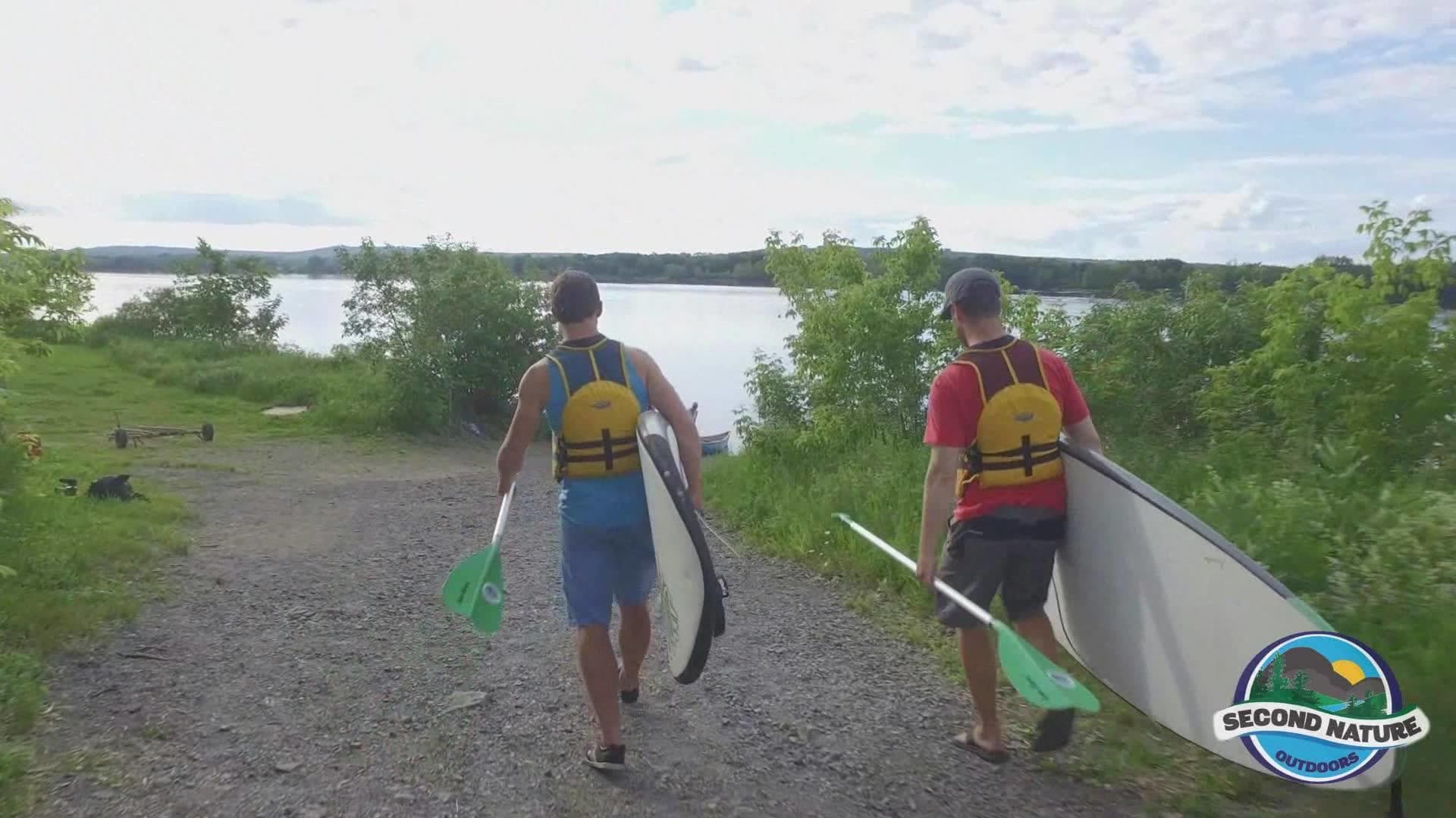 Two paddlers carrying canoe to lakeshore on gravel path