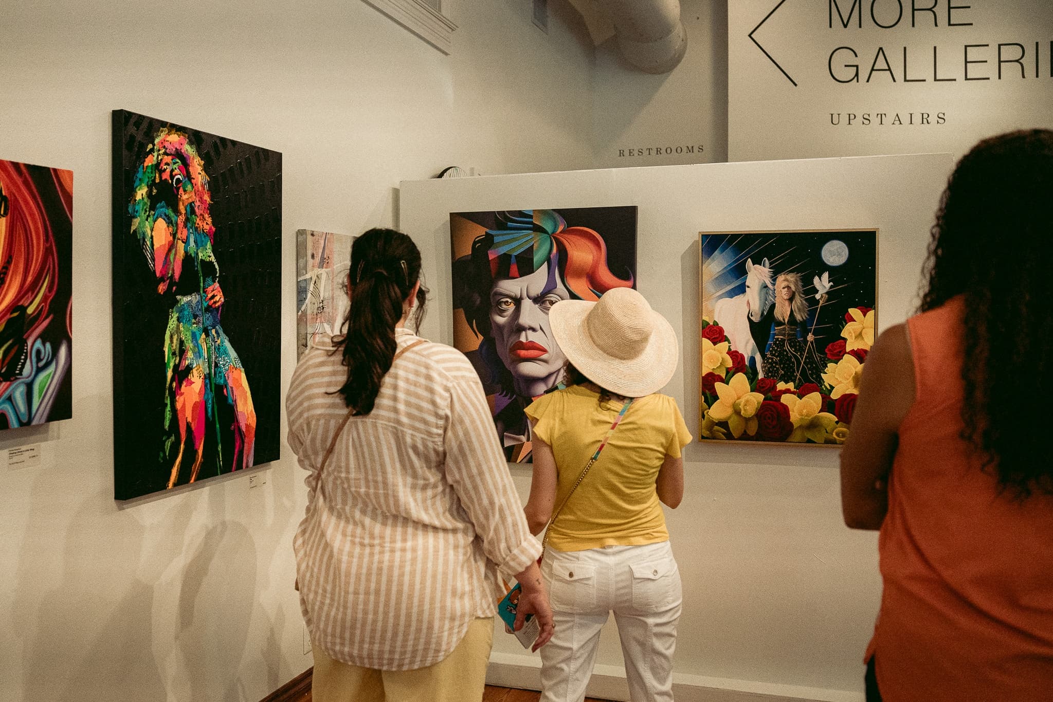 Visitors viewing vibrant paintings in indoor art gallery exhibit