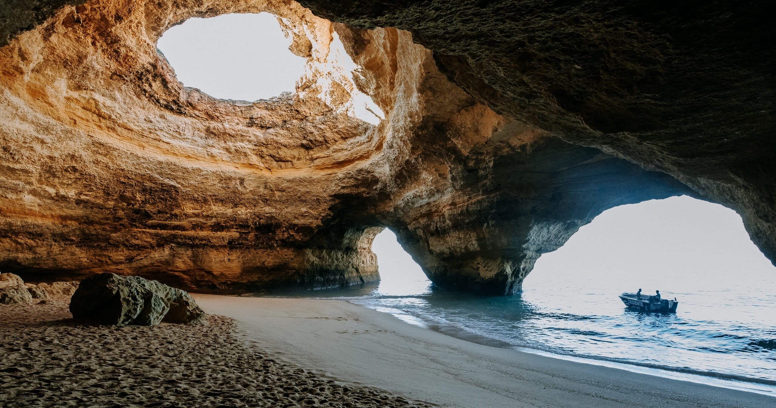 Sea cave with sandy beach and anchored tour boat in grotto
