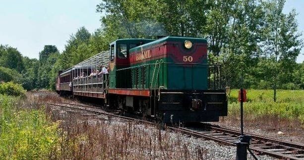 Green locomotive traveling rural tracks across fields near Maine