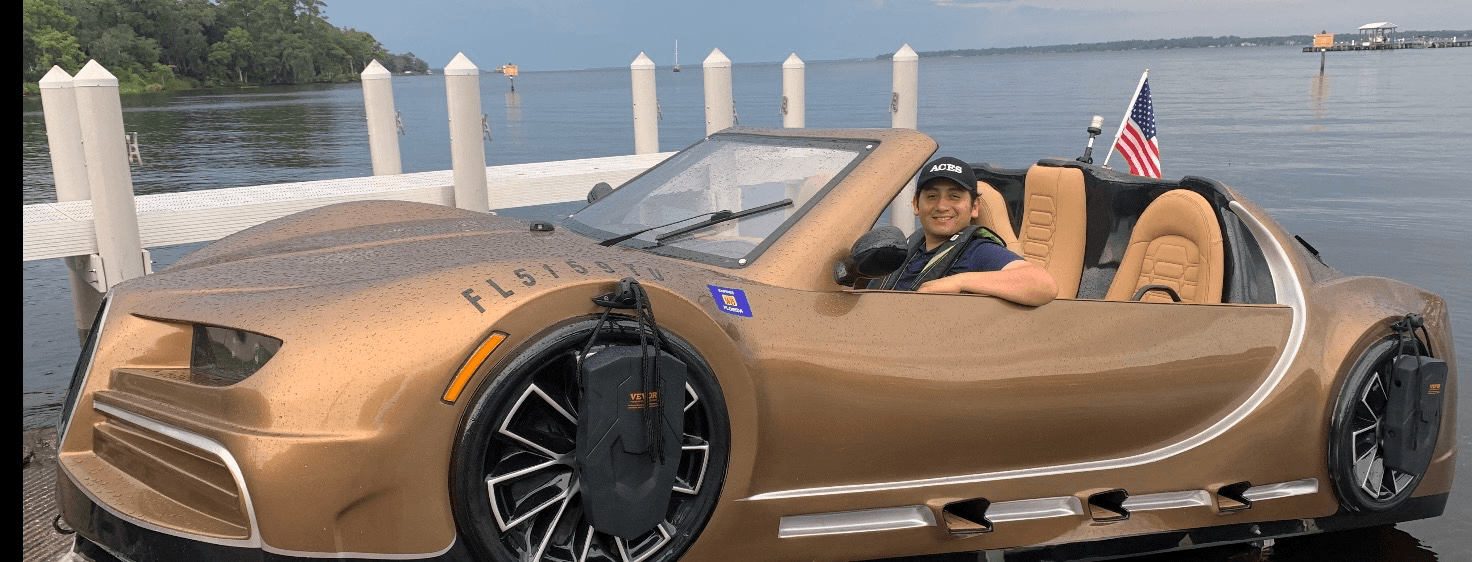 Gold amphibious sports car parked at marina with passenger onboard