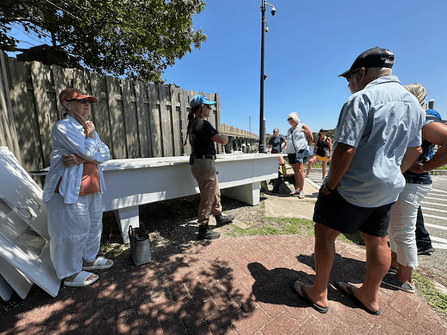 Visitors on coastal oyster farm tour by waterfront in sunlight