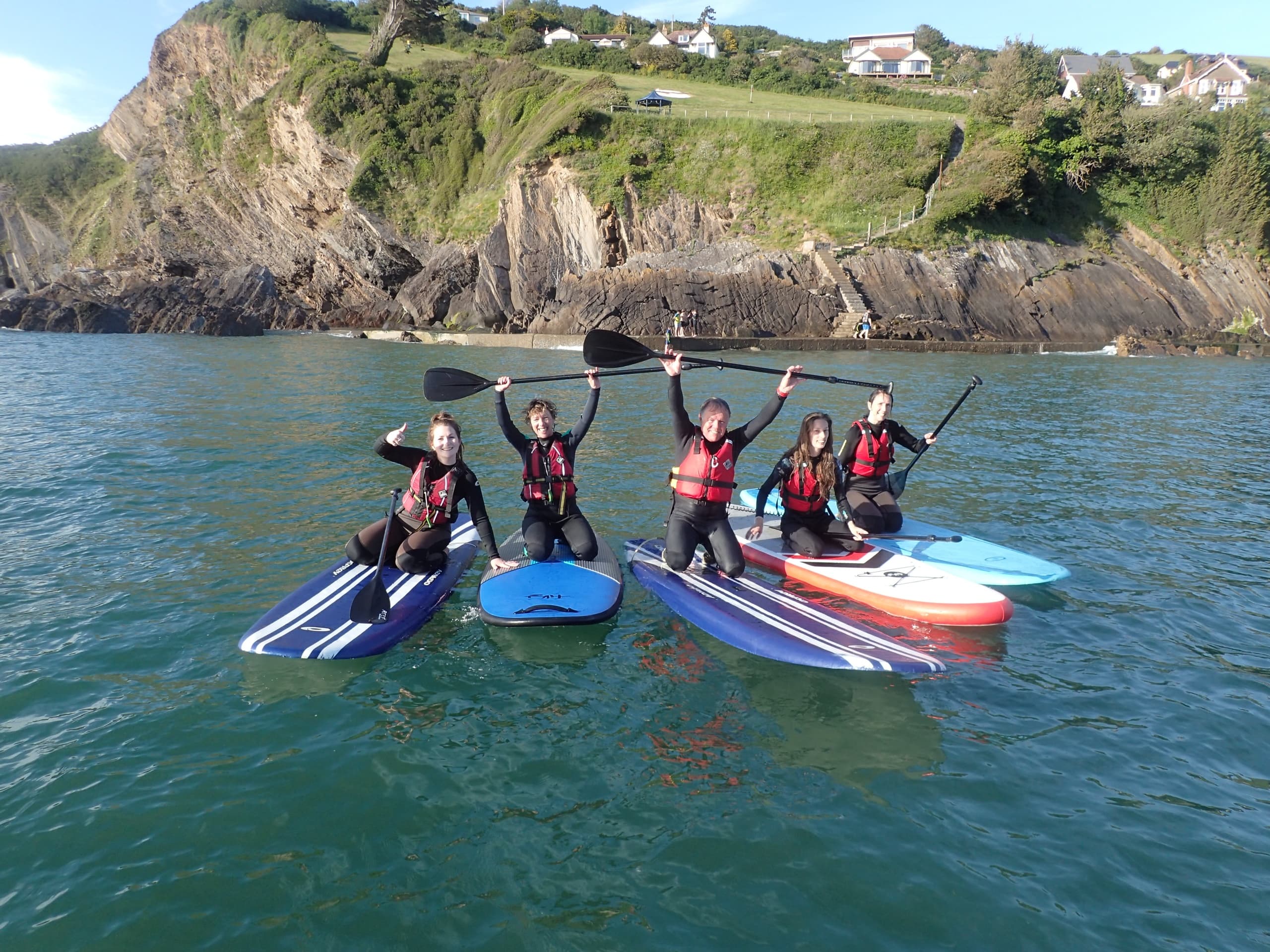 Group of paddleboarders cheering off rocky bay, coastal adventure