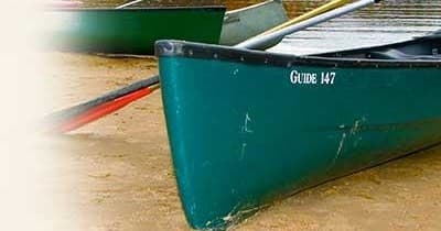 Green canoe on lakeshore ready for paddling on calm water