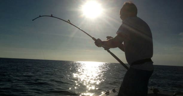 Angler silhouette battling fish at sea at sunset