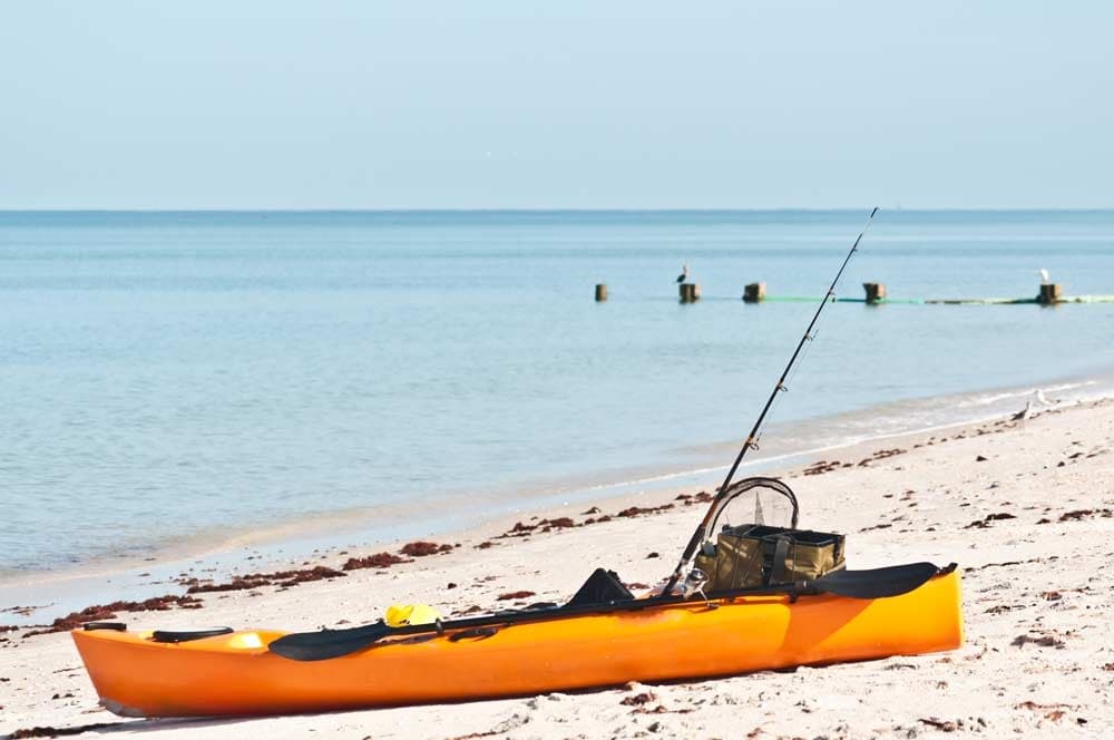 Fishing kayak resting on white sand beach by clear ocean