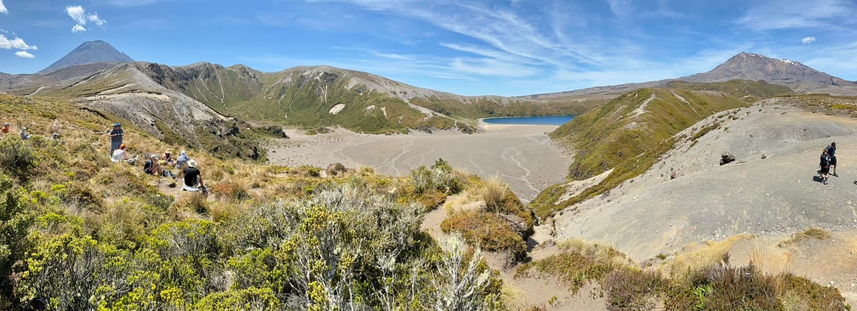 Panoramic volcanic alpine hike across tussock basin with lake