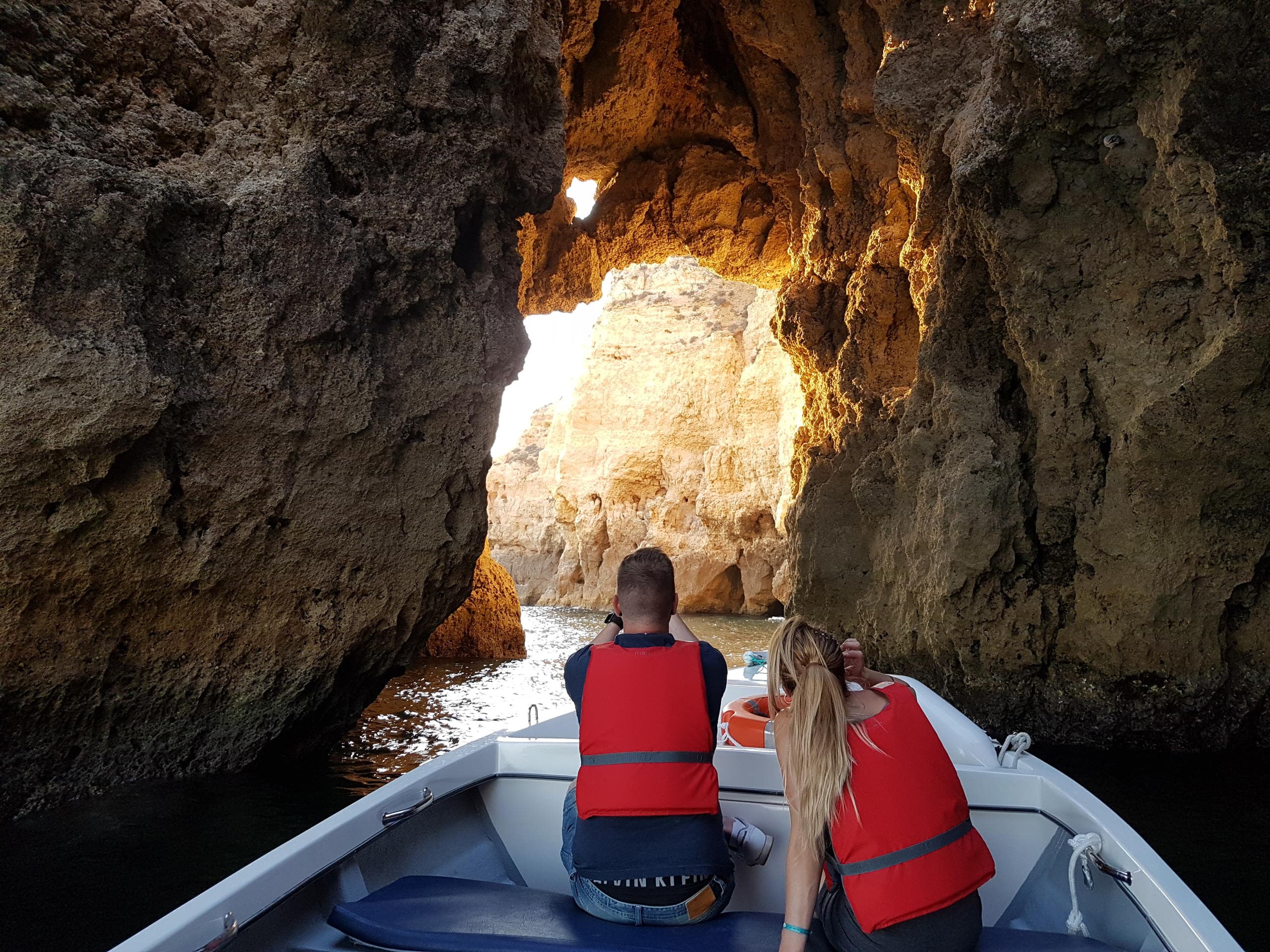 Boat tour entering dramatic sea cave among golden cliffs