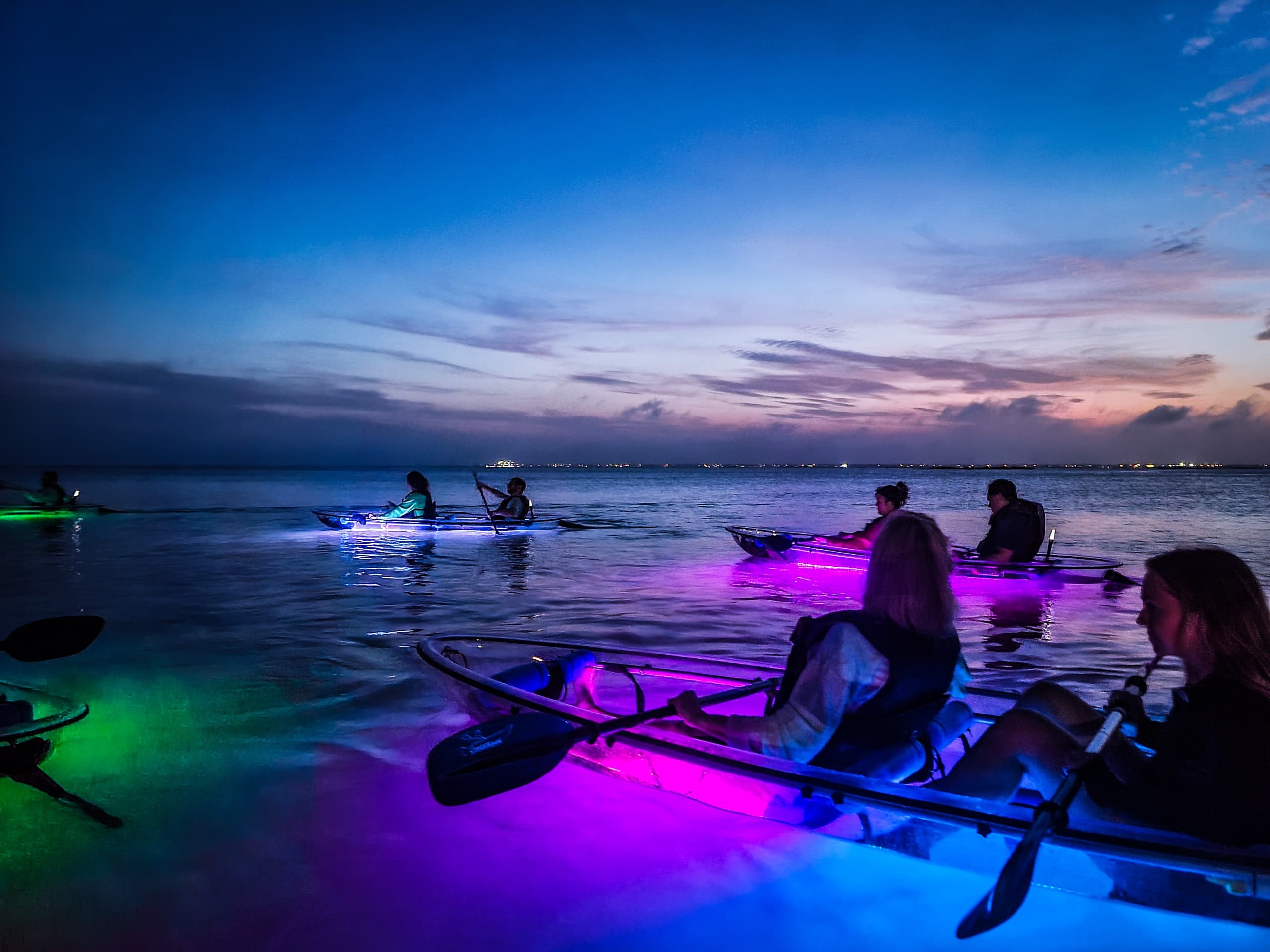 Paddlers kayaking at twilight with colorful LED lights