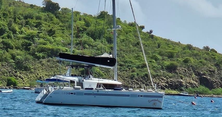 Catamaran moored near green hillside in coastal waters