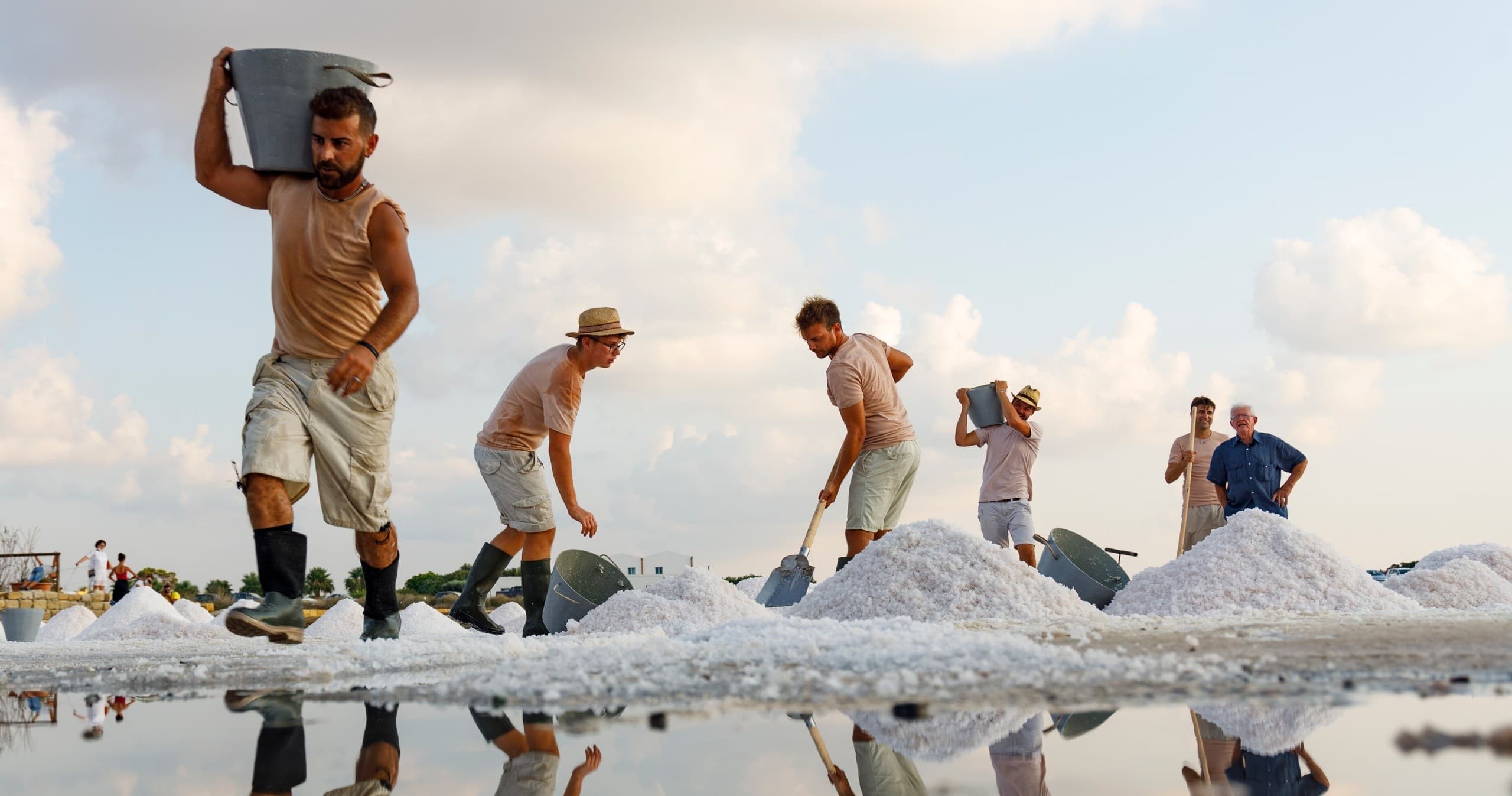 Workers harvesting salt on reflective coastal salt pans