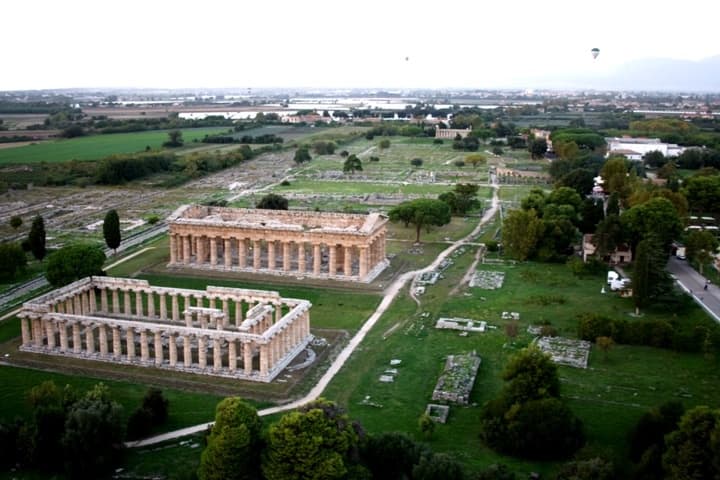 Ancient Paestum temples aerial view amid green fields, ruins