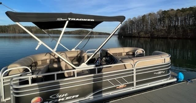 Pontoon boat docked on calm lake with wooded shoreline