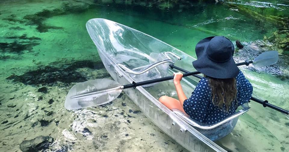 Top-down transparent kayak over turquoise spring, woman paddling