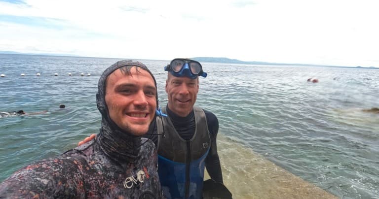 Freedivers smiling on rocky pier with open ocean horizon in background