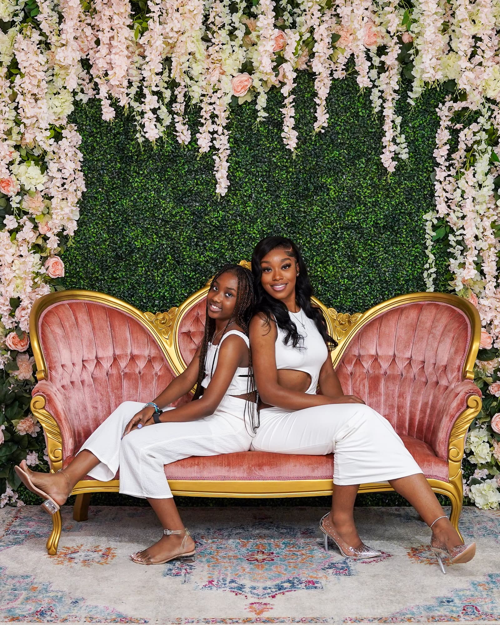 Two women seated on floral garden sofa backdrop in studio