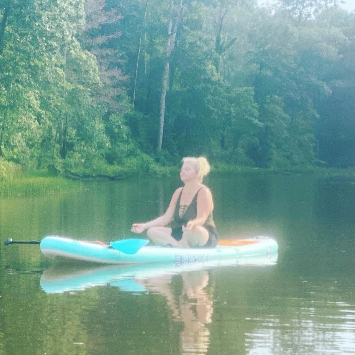 Meditative paddleboard yoga seated on calm reflective lake
