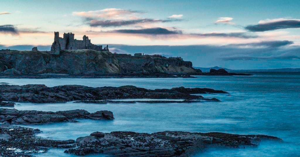 Coastal castle ruins at dusk with rocky tide pools and sea