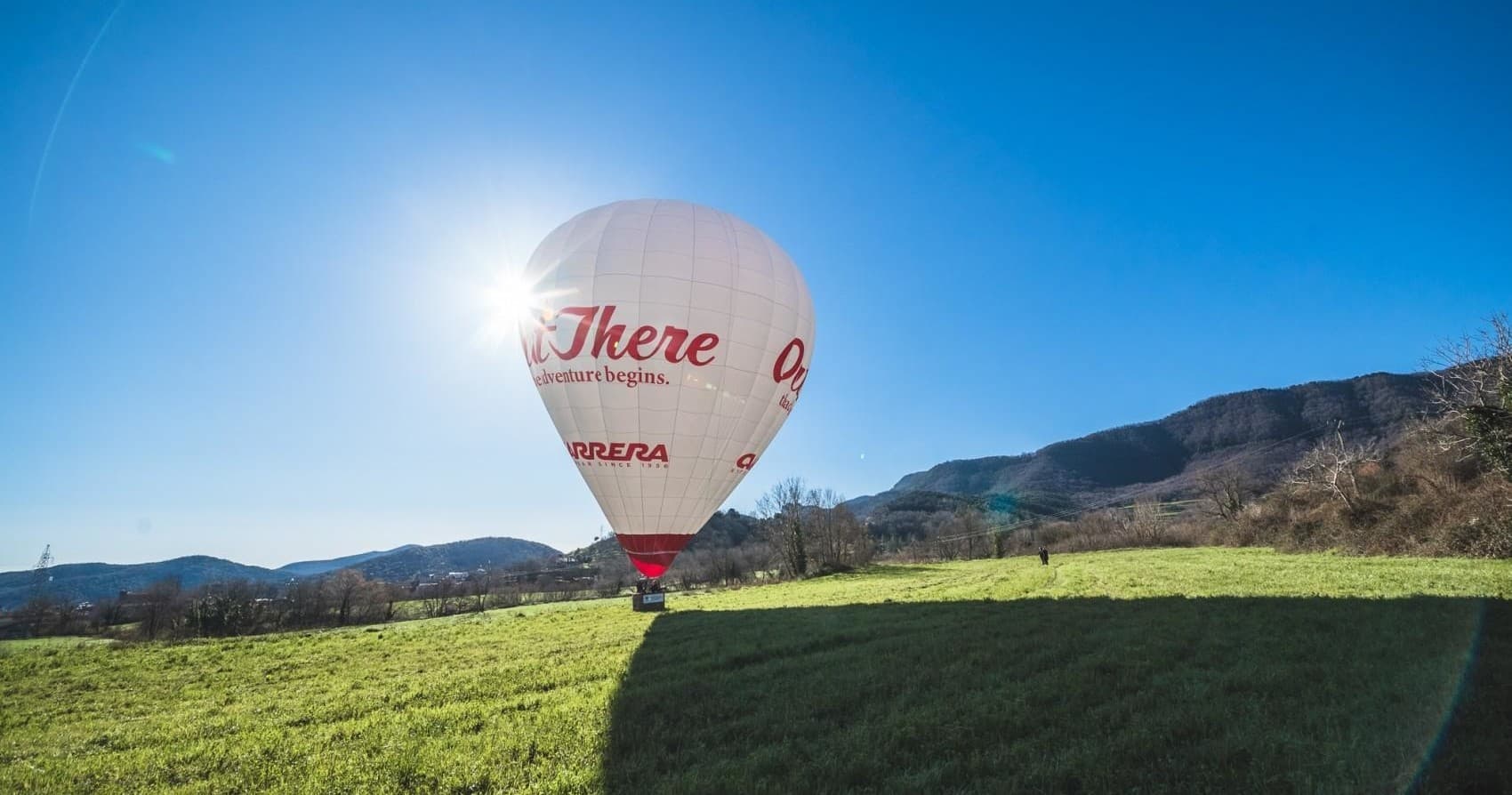 Single hot air balloon glowing with sun flare over rural landscape