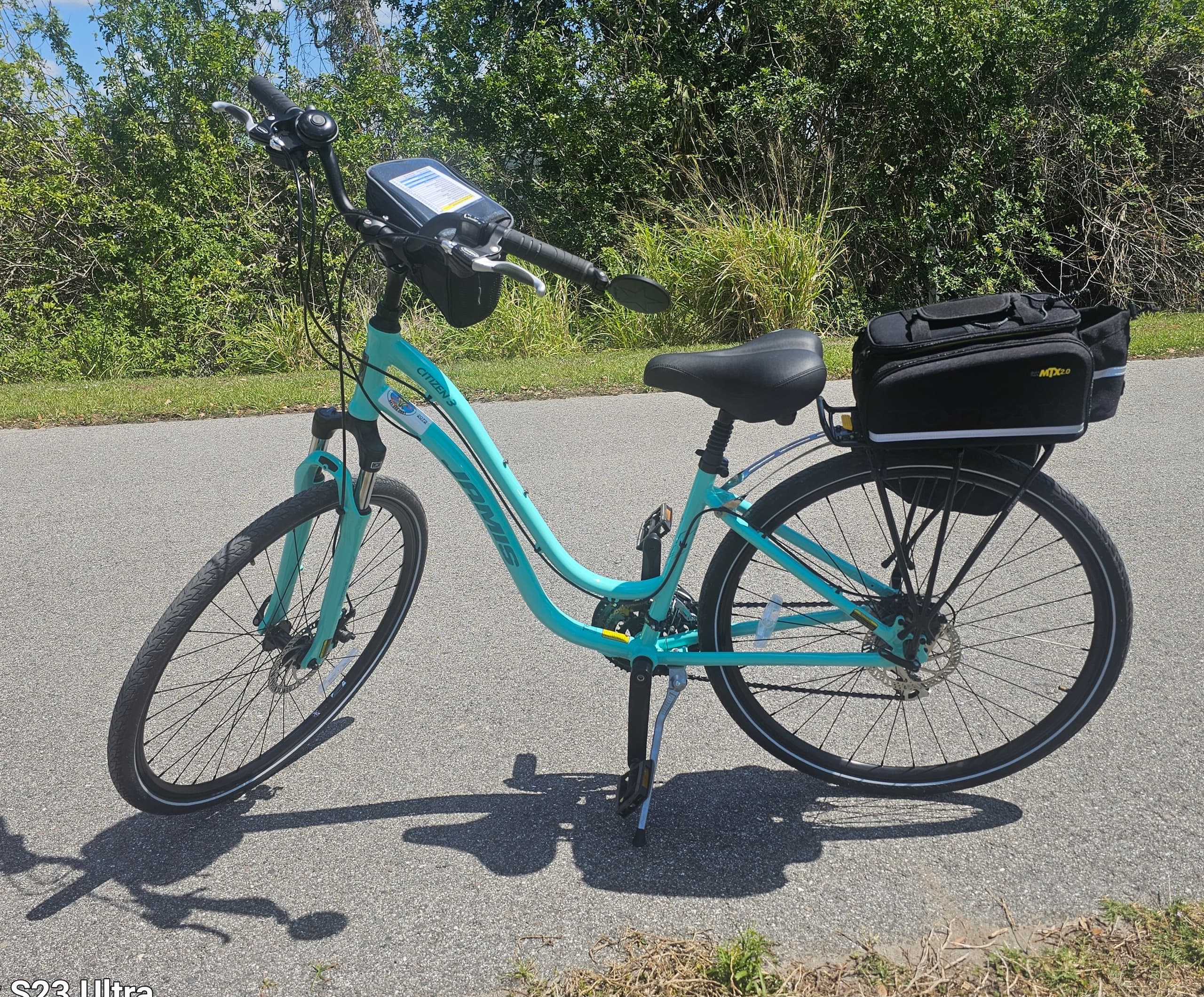 Teal cruiser bike on paved trail with green foliage backdrop
