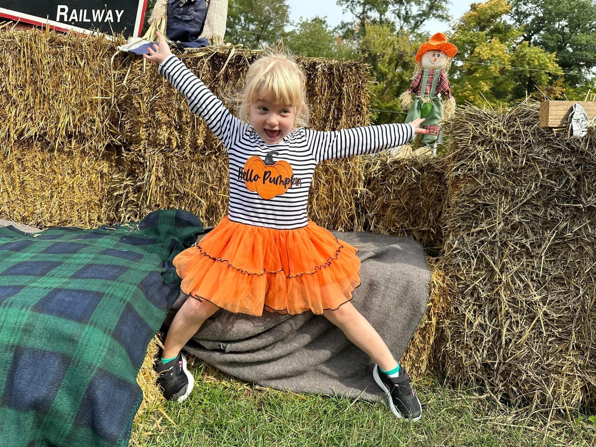 Child in pumpkin costume on hay bale at autumn railway event