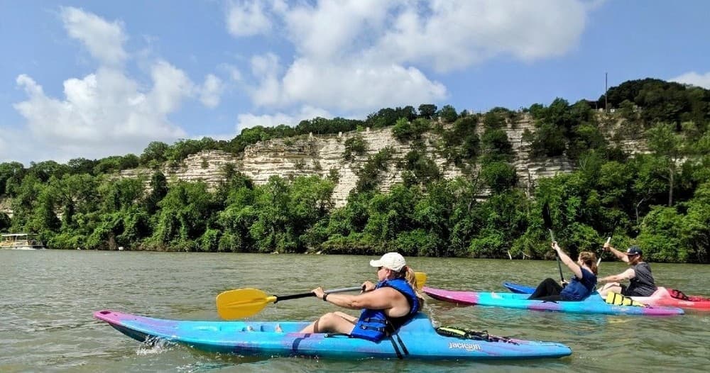 Kayakers paddling near limestone bluffs on sunny day outing