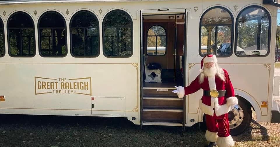 Santa waving by classic trolley exterior at outdoor Raleigh tour stop