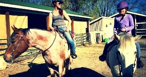 Two riders horseback riding on Trinity River Farm ranch under sunny skies