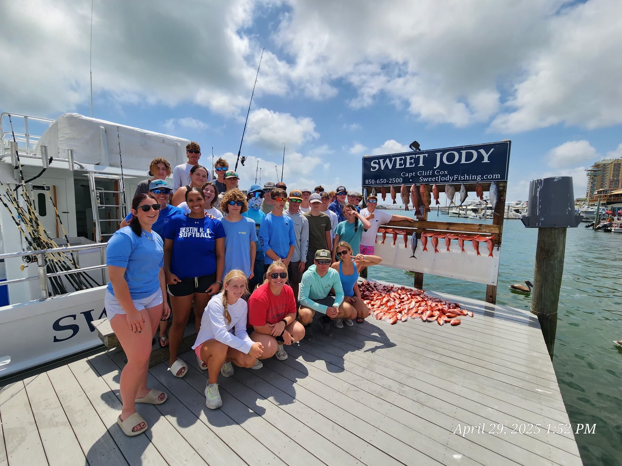 Fishing charter group posing on marina dock with catch under Sweet Jody sign