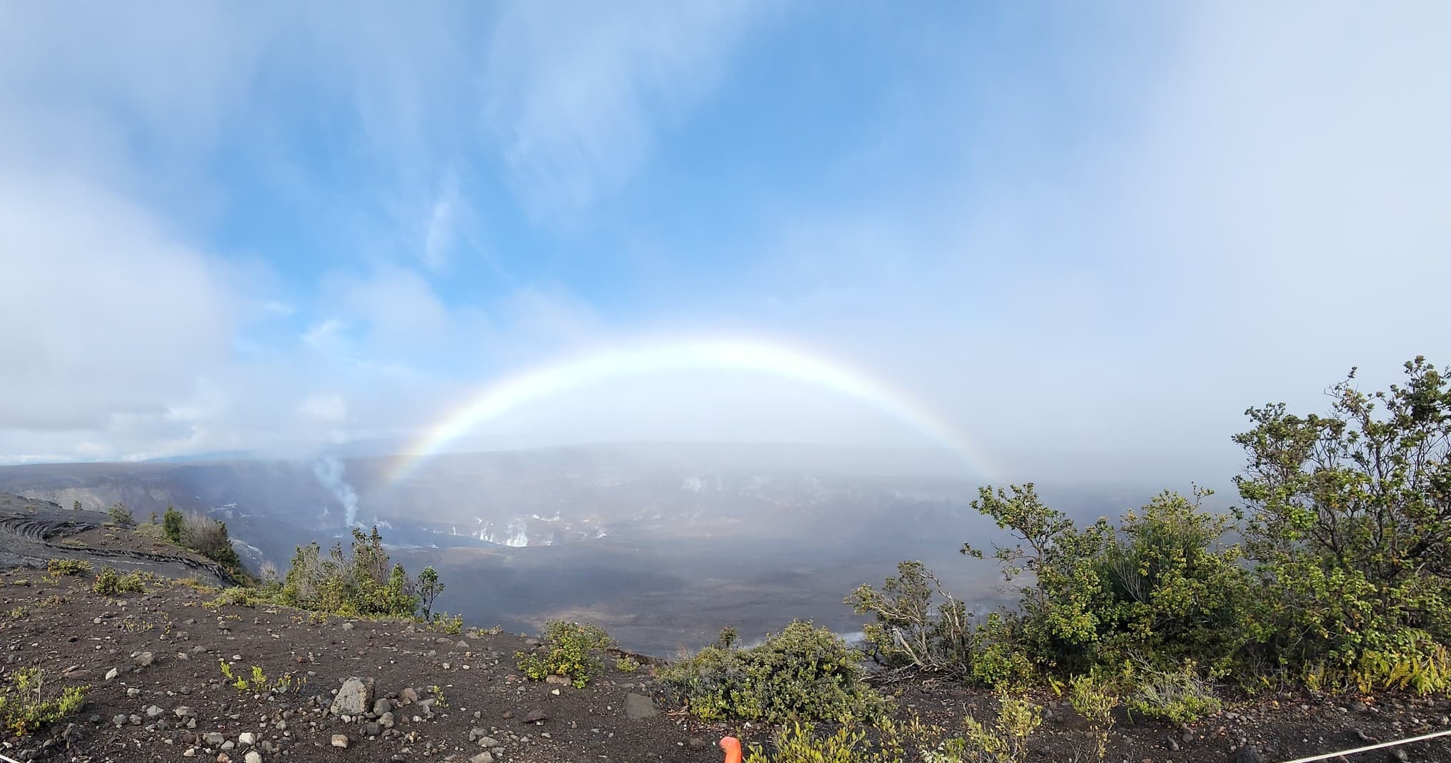 Full rainbow over coastal volcanic terrain and low shrubland