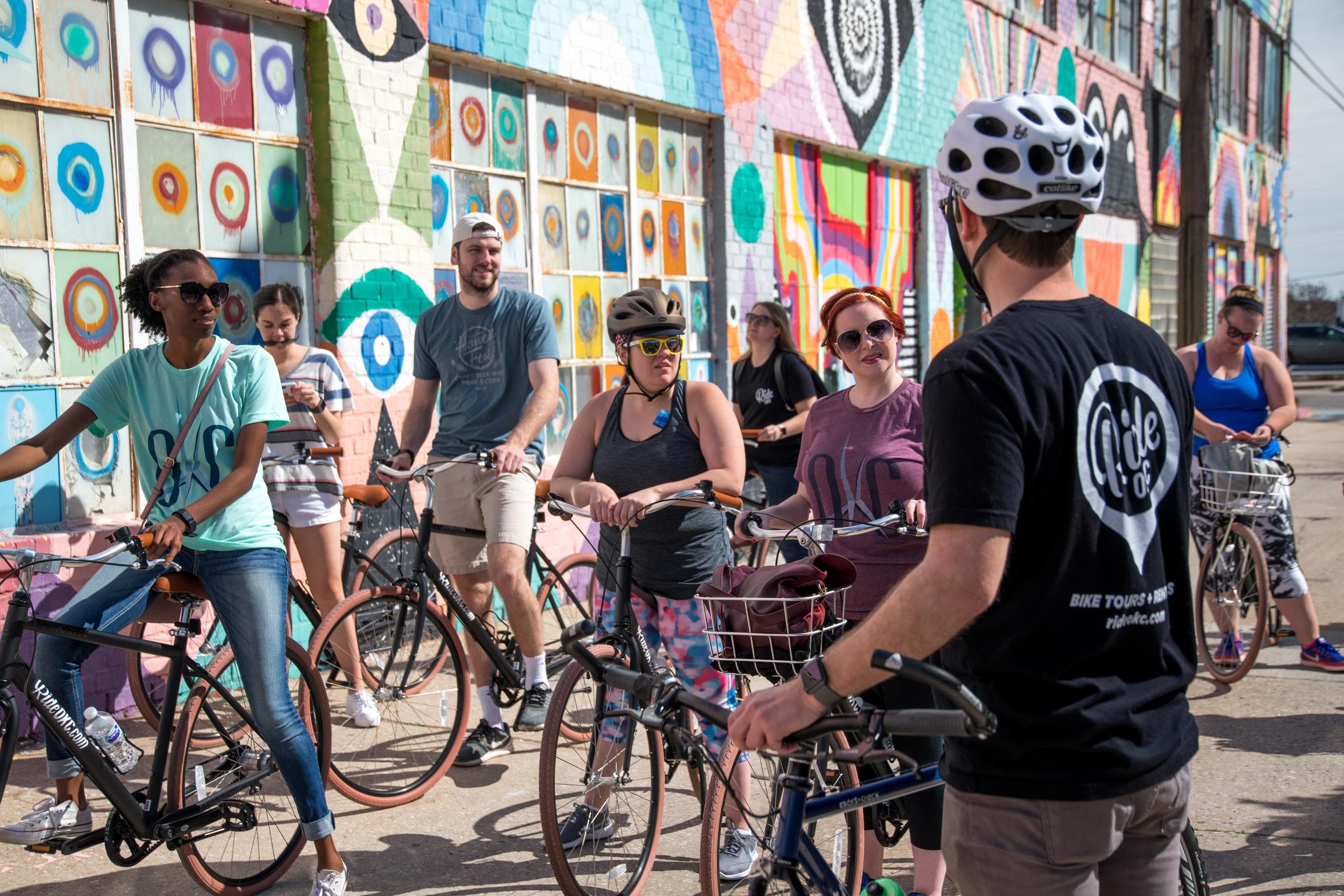 Large bike ride crowd posing before vibrant street art mural
