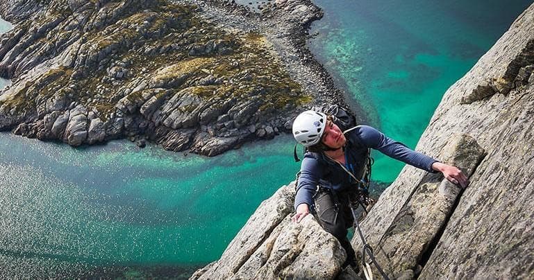 Climber scaling sea cliff above turquoise fjord, dramatic