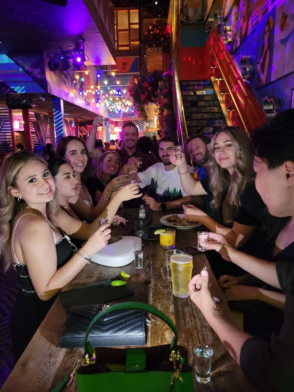 Large group toasting at vibrant neon-lit bar and long table indoors