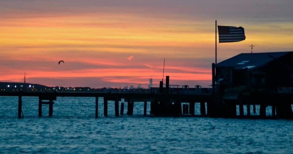 Sunset pier silhouette with American flag over tranquil coastal waters