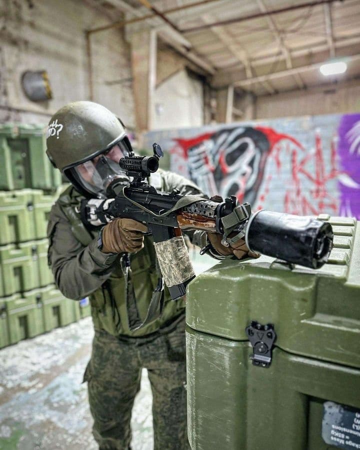 Airsoft player aiming rifle behind crate in indoor arena
