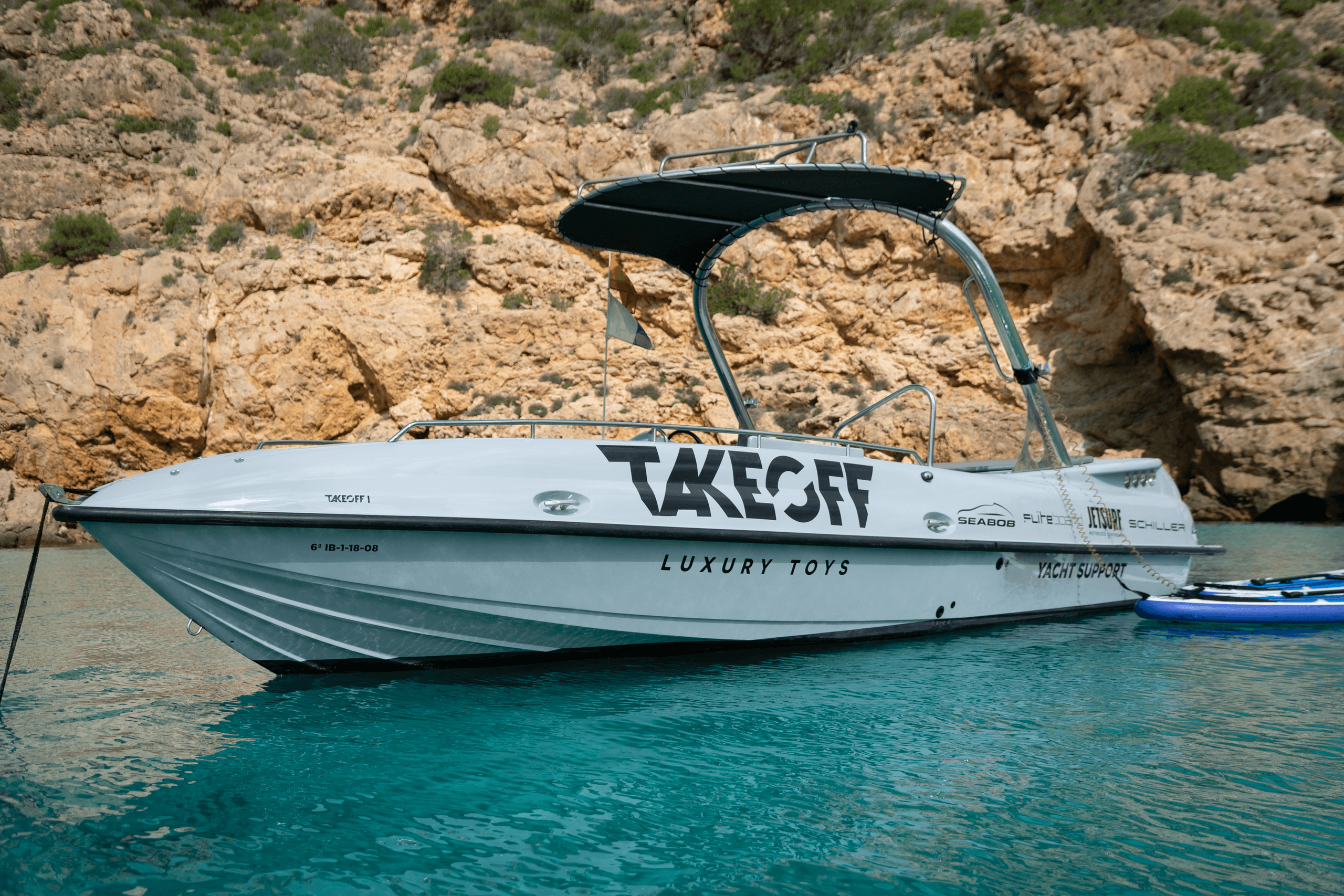 Powered boat TAKEOFF moored in crystal bay with sunlit cliffs