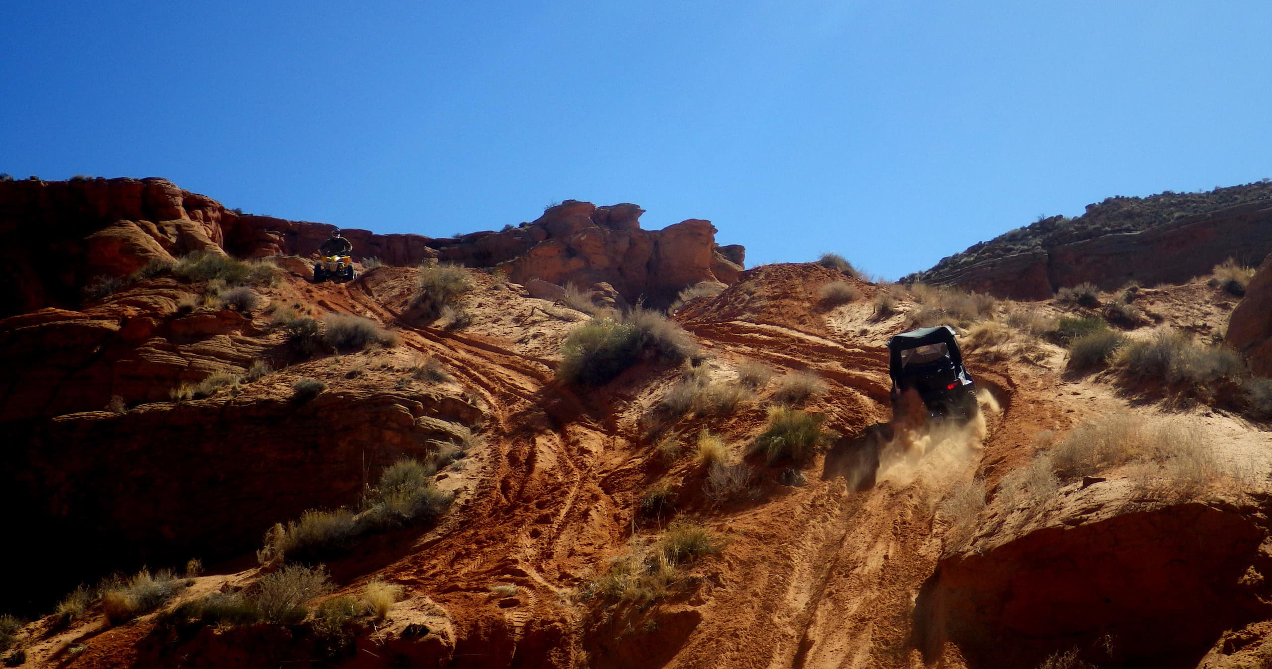 UTV climbing steep red-rock trail under blue sky, off-road action